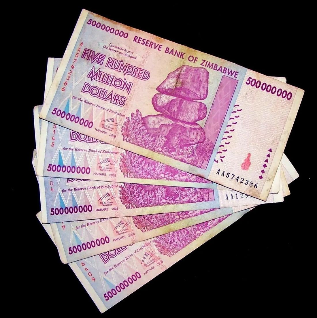 Stack of Zimbabwe 500 million dollar banknotes with purple design and balancing rocks.