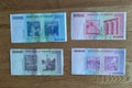 Four Zimbabwean banknotes on wood surface, displaying Reserve Bank of Zimbabwe currency