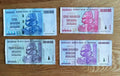 Four Zimbabwe banknotes of high denominations arranged on a wooden surface, featuring rocks motif.
